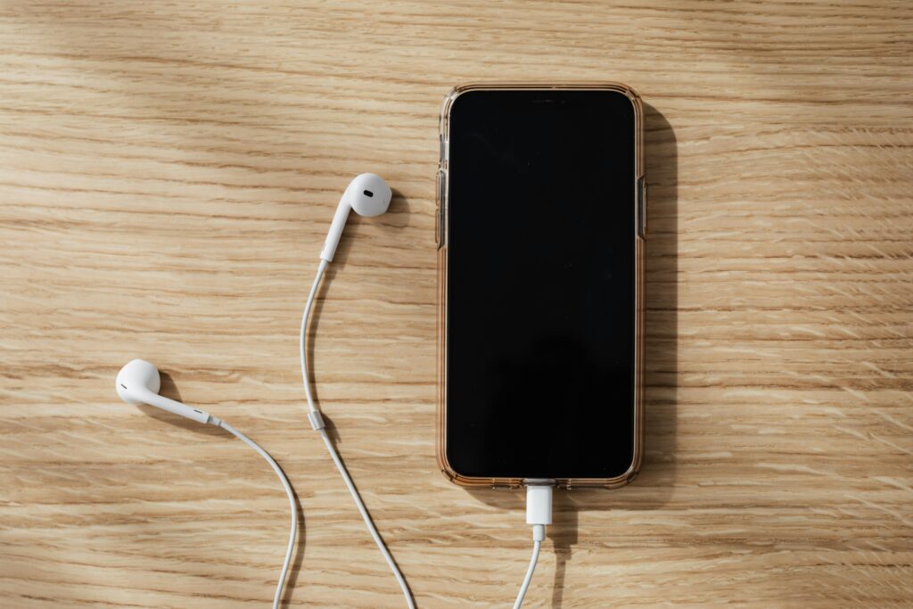 iPhone with corded headphones plugged in on a woodgrain background